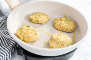 Final batch of zucchini fritters cooking in a shallow skillet on medium heat.