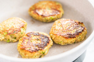Zucchini cakes being seared in a nonstick skillet until golden.