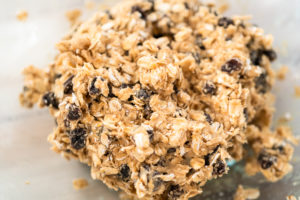 Textured oatmeal raisin cookie dough shown in a mixing bowl, highlighting rolled oats and raisins.