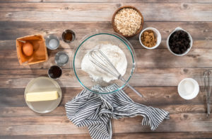 Flat lay of peanut butter cookie ingredients, including butter, sugars, flour, and eggs, in clear mixing bowls.