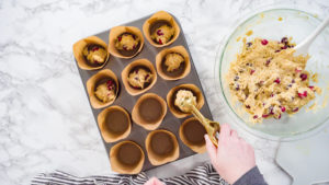 Flat lay. Step by step. Scooping dough into tulip muffin liners with mixture scoop to bake cranberry muffins.