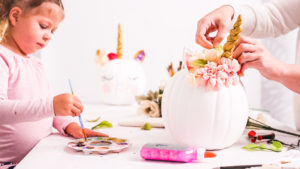 Mother and daughter decorating craft pumpkins with unicorn theme for Halloween.