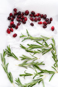 Covering fresh cranberries and rosemary in sugar to decorate chocolate bundt cake with chocolate frosting.