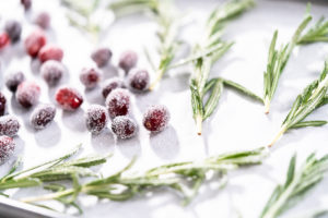 Covering fresh cranberries and rosemary in sugar to decorate chocolate bundt cake with chocolate frosting.