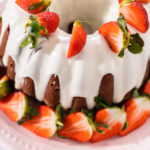 Cream cheese frosting drizzled over red velvet bundt cake with strawberries