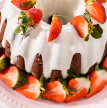 Cream cheese frosting drizzled over red velvet bundt cake with strawberries