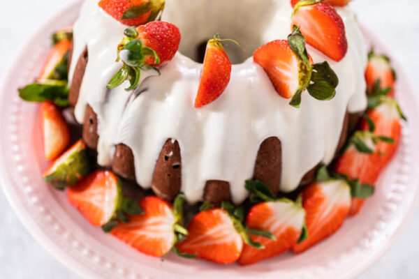 Red velvet bundt cake - Arina Photography Cream cheese frosting drizzled over red velvet bundt cake with strawberries