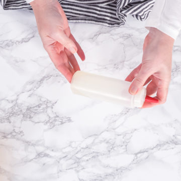 Filling a clean squeeze bottle with cooled homemade syrup on a white marble countertop.