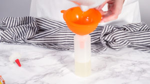 Orange funnel inserted into squeeze bottle standing on counter with striped towel.