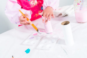 Child painting facial features on a unicorn craft roll using a small paintbrush.