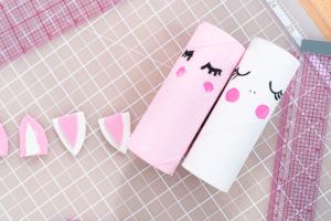 Close-up of two painted paper rolls with eyelashes and blush drying next to cut-out unicorn ears.