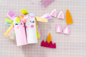Flat lay of colorful unicorn toilet paper roll crafts with tissue paper manes and cutout ears and horns.