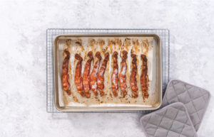 Cooking bacon strips - Arina Photography Finished tray of baked bacon resting on white parchment paper.