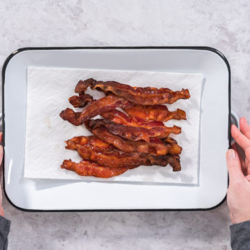 Cooking bacon strips - Arina Photography Hands holding a tray of crispy, baked bacon strips on parchment paper.