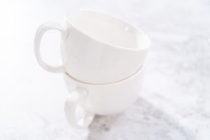 Chocolate mug cake - Arina Photography Two stacked white microwave-safe mugs with handles, set on a marble counter.