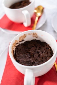 Chocolate mug cake - Arina Photography Close-up of warm Nutella mug cake in a white cup on red napkin with gold spoon, fresh out of the microwave.