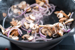 Spinach and ham frittata - Arina Photography Mushrooms and thin red onion slices sizzling in a skillet, part of frittata prep.