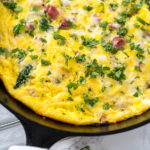 Full spinach and ham frittata in black skillet showing cheesy, golden surface with greens and ham.