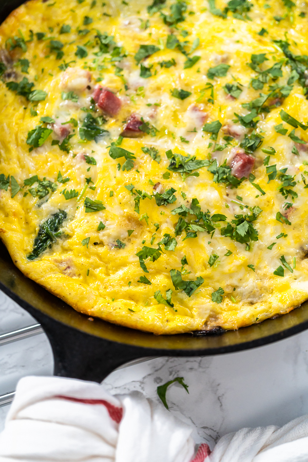 Full spinach and ham frittata in black skillet showing cheesy, golden surface with greens and ham.