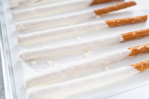 Pretzel rods coated in white candy melt, neatly arranged on parchment paper to cool and set.