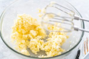 Creamed butter and sugar in a glass bowl with beaters overhead, showing light and fluffy texture for cake batter.