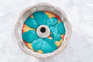 Red, white, and blue cake batter layered in a floured Bundt pan before baking.