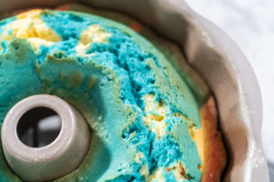 Close-up of freshly baked red, white, and blue Bundt cake still in the pan with a cracked blue top.
