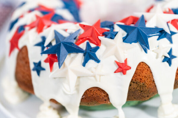 July 4th bundt cake - Arina Photography Close-up of a patriotic Bundt cake topped with glossy vanilla glaze and red, white, and blue chocolate stars.