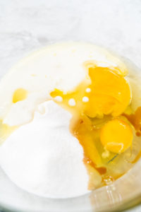 Close-up of eggs, sugar, vanilla extract, oil, and buttermilk in a glass bowl, ready to be mixed for cupcake batter.