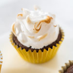 Chocolate cupcake in a gold liner topped with toasted marshmallow meringue frosting, swirled and lightly golden from a kitchen torch.