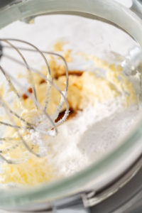 Whipping strawberry buttercream frosting in a stand-alone electric mixer with a whisk attachment.
