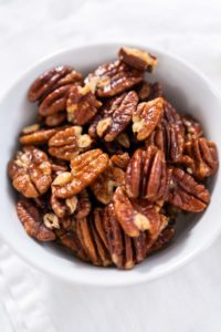 Freshly toasted pecans in a small white bowl.