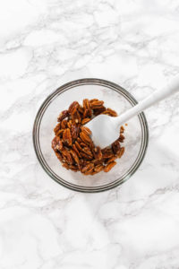 Mixing ingredients in a large glass mixing bowl to make toasted pecans.