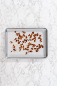 Spreading organic pecans on a baking sheet lined with parchment paper to make toasted pecans.