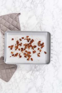 Freshly toasted pecans on a baking sheet lined up with parchment paper.