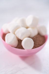 Filling in pink chocolate shells with hot chocolate mix and mini marshmallows to prepare hot chocolate bombs.