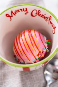 Preparing Christmas hot chocolate bombs with hot milk in a Christmas mug.