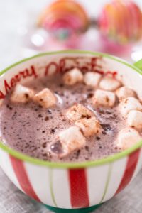 Preparing Christmas hot chocolate bombs with hot milk in a Christmas mug.