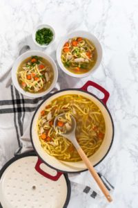 Flat lay. Serving chicken noodle soup with kluski noodles in white ceramic soup bowls.