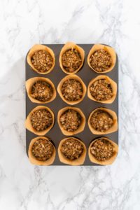 Flat lay. Scooping dough with dough scoop into cupcake pan lined with tulip paper muffin liners to bake banana oatmeal muffins.
