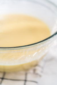 White chocolate ganache frosting - Arina Photography Whisking in a large glass bowl together ingredients to make the white chocolate ganache frosting.