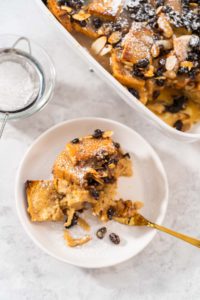 Bread pudding - Arina Photography Serving freshly baked bread pudding with raising and almond slivers in a white casserole dish.