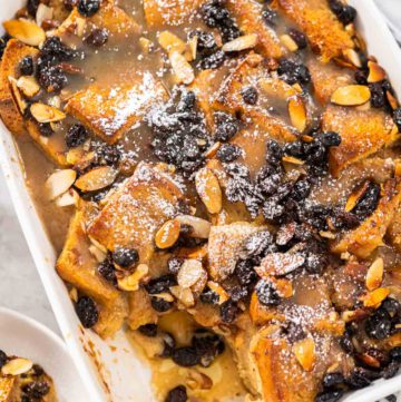 Bread pudding - Arina Photography Serving freshly baked bread pudding with raising and almond slivers in a white casserole dish.