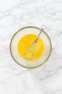 Lemon Wedge Cookies - Arina Photography Egg yolks whisked in small bowl on marble counter.