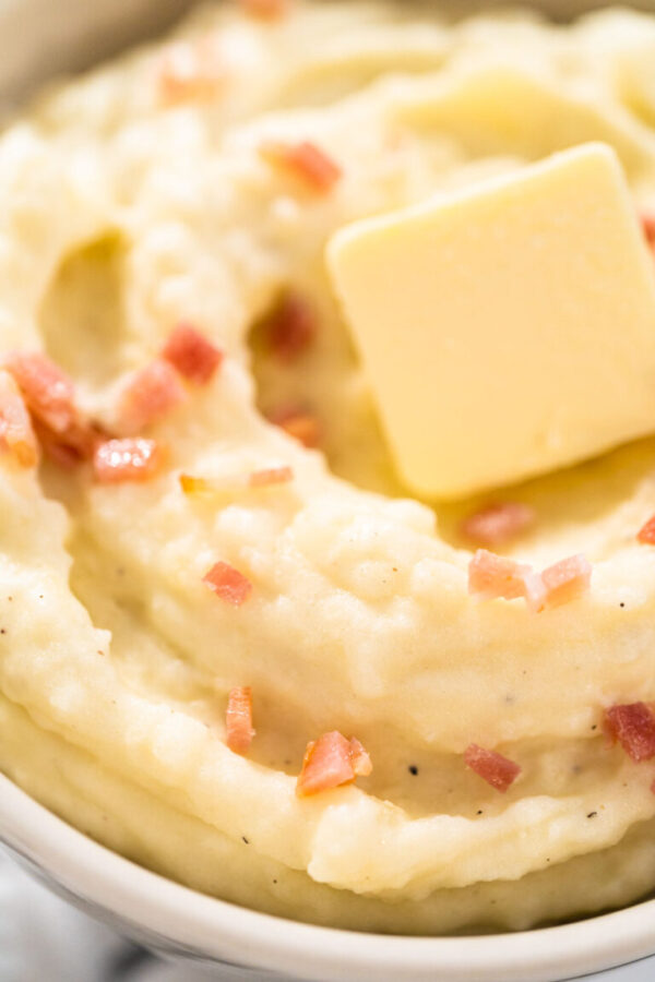 Mashed potatoes - Arina Photography Mashed potatoes. Creamy mashed potatoes garnished with a slice of butter and bacon bits in a bowl.