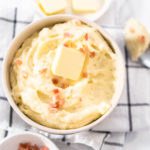 Mashed potatoes. Creamy mashed potatoes garnished with a slice of butter and bacon bits in a bowl.