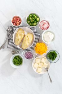Pressure Cooker Baked Potatoes - Arina Photography Flat lay. Pressure Cooker Baked Potatoes. Garnished large baked potatoes with butter, sour cream, cheese, and bacon bits on a white plate.