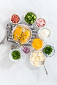 Pressure Cooker Baked Potatoes - Arina Photography Flat lay. Pressure Cooker Baked Potatoes. Garnished large baked potatoes with butter, sour cream, cheese, and bacon bits on a white plate.