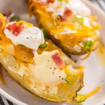 Pressure Cooker Baked Potatoes. Garnished large baked potatoes with butter, sour cream, cheese, and bacon bits on a white plate.