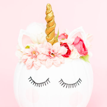 White unicorn pumpkin decorated with flowers on a pink background.